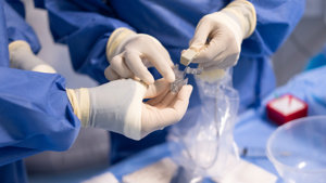 The gloved hands of two interventional radiologists handling medical equipment