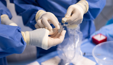 The gloved hands of two interventional radiologists handling medical equipment