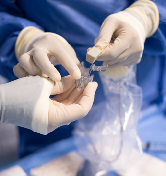 The gloved hands of two interventional radiologists handling medical equipment