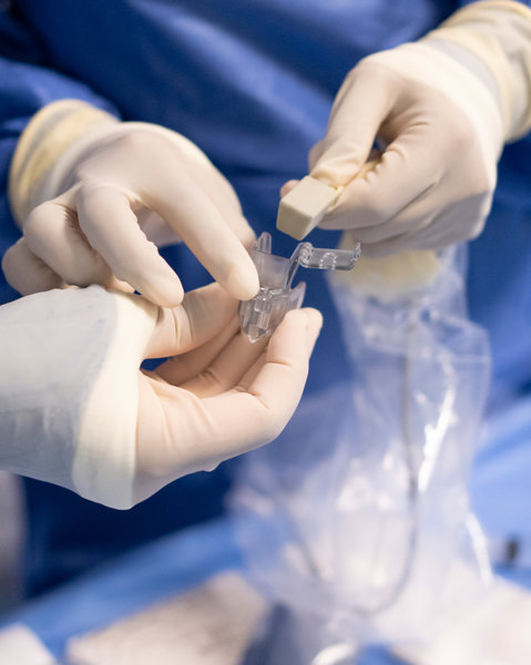 The gloved hands of two interventional radiologists handling medical equipment