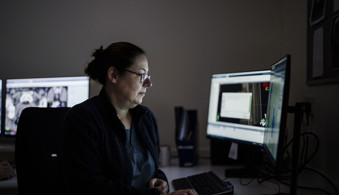 Female oncologist sitting at a desk looking at computer screens.